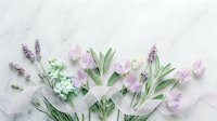 Soft pastel flowers with lavender, tulips, and green leaves arranged on white marble with a delicate ribbon, flat lay style.