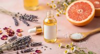 Natural aromatherapy essential oil bottle with fresh grapefruit, lavender flowers, rose petals and sea salt on pink background for spa wellness treatments.