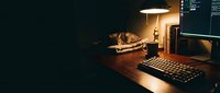 Workspace with mechanical keyboard, monitor, and desk lamp illuminating wooden surface at night for gaming or creative work.