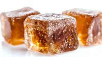 Amber-colored sugar candy cubes dusted with powdered sugar on white background, macro close up view showing crystalline texture and translucent glow.