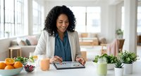 Professional African American businesswoman using tablet in modern bright office kitchen with fresh vegetables and healthy lifestyle elements.