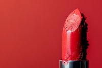 Damaged red lipstick bullet with smudged texture and bite marks against vibrant red background, showcasing raw beauty and artistic cosmetic still life.