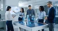 Diverse business team collaborating around interactive digital table in modern office conference room during strategic planning meeting.