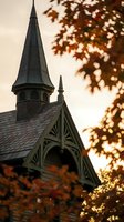 Historic wooden church steeple with ornate Gothic architecture framed by autumn foliage during golden hour sunset creating warm atmospheric lighting.