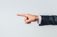 Male hand in business suit sleeve pointing finger to side against light background, professional gesture showing direction or blame.