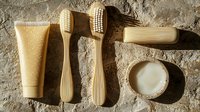 Eco-friendly bamboo toothbrushes with natural toothpaste and salt on textured stone background, sustainable dental care concept in warm beige tones.