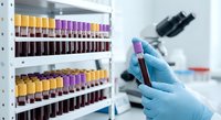 Medical laboratory technician in blue gloves holding blood sample tube with organized test tubes rack in clinical diagnostic facility for analysis.