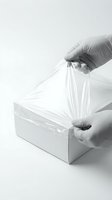 Person wearing protective latex gloves placing clear plastic bag over white cardboard box for packaging, shipping, and storage protection purposes.