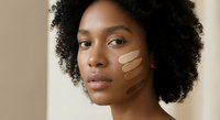 Young African American woman with curly hair testing foundation shades on cheek for perfect skin tone match in beauty routine.