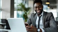 Successful African American businessman in grey suit working with laptop and smartphone in modern office, perfect for business, success, and workplace diversity concepts.
