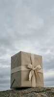 Rustic linen-wrapped gift box with a bow on a rocky surface against a dramatic cloudy sky, evoking natural elegance and minimalist style.