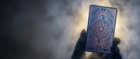 Hand holding ornate tarot card with mystical blue design against dramatic cloudy sky background for fortune telling and spiritual guidance sessions.