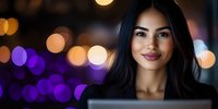 Young Asian woman smiling at laptop screen in evening, illuminated by purple and golden bokeh lights background, radiating positive professional energy.