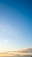 Clear blue sky with soft white clouds at horizon during golden hour sunset creating peaceful atmospheric background for nature and weather concepts.