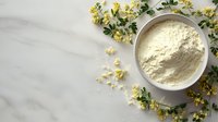 Natural organic flour in ceramic bowl surrounded by fresh yellow wildflowers on white wooden background for healthy baking and cooking recipes.