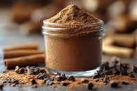 Ground cinnamon powder in glass jar with scattered spices, cinnamon sticks and cloves on rustic wooden surface, macro food photography.