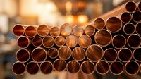 Stack of copper pipes in warehouse with warm industrial lighting for construction and plumbing projects in manufacturing facility.