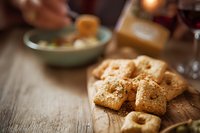 Homemade savory crackers with herbs and spices on rustic wooden board, cozy dinner setting with wine glass and food in background.