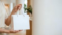 Close-up of person holding blank white shopping bag with handles in bright interior space, suitable for branding and retail marketing mockups.
