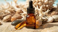 Amber glass dropper bottle with essential oil on beach sand surrounded by seashells and stones, warm sunlight creating relaxing spa atmosphere.