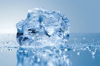 Melting ice chunk with crystalline structure on wet reflective surface against light blue background, water droplets creating natural mirror effect and bokeh.