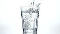 Clear glass filled with splashing water creating dynamic motion and bubbles against clean white background for refreshing beverage concepts.