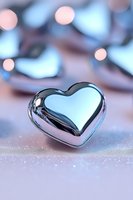 Metallic heart shape on soft pink surface with dreamy bokeh lights background creates romantic mood for Valentine's Day cards and love concepts.