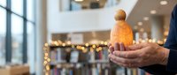 Mature man holding golden knitted figurine in modern shopping mall with festive lights, representing holiday charity, giving, and seasonal generosity during winter celebrations.