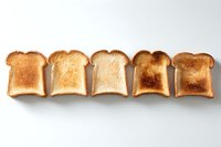 Five slices of toasted white bread showing different levels of browning from light to dark, arranged in row on white background, isolated food photography.