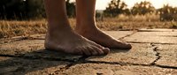Barefoot person standing on cracked, dry asphalt road during drought conditions, symbolizing environmental crisis, climate change, and water scarcity issues.