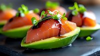 Fresh salmon sashimi served in avocado boats garnished with microgreens and soy sauce on dark slate plate, elegant appetizer presentation for fine dining.