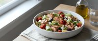 Fresh Mediterranean quinoa salad with roasted vegetables, feta cheese and herbs in white bowl on wooden table. Healthy lunch meal with olive oil dressing.
