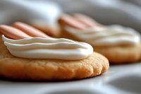 Freshly baked cookies topped with creamy white frosting, arranged on a white plate. Perfect for bakery, dessert, and food photography projects.