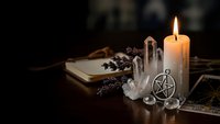 Mystical altar setup with burning candle, crystal cluster, pentagram pendant and dried herbs on wooden surface for spiritual practices and witchcraft rituals.