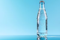 Clear glass bottle with sparkling water on blue background, refreshing drink with bubbles and condensation droplets, minimalist beverage photography.