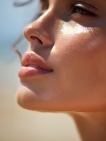 Close up profile view of glowing sun-kissed skin with natural makeup, highlighting dewy complexion and plump lips against soft blurred background.