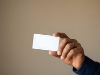 Hand holding blank white business card against neutral beige background, suitable for branding, corporate identity, and marketing mockup designs.