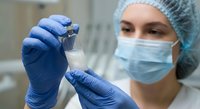Female laboratory technician in protective equipment examining test tube sample in medical research facility for scientific analysis and healthcare diagnostics.