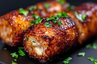 Crispy bacon-wrapped chicken breast rolls filled with melted cheese and garnished with fresh herbs on dark background, macro food photography.