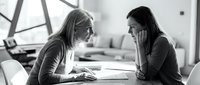 Two professional women having focused business discussion at modern office table in black and white photography for corporate communication concepts.
