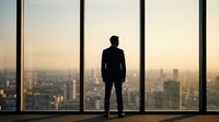 Professional businessman silhouette standing at office window overlooking city skyline at sunset, corporate success and leadership concept for business.