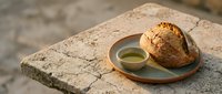 Freshly baked round loaf of artisan bread with olive oil on wooden plate, rustic stone surface, Mediterranean cuisine and cooking concept.