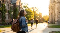 Young Asian female college student with backpack walking on university campus during golden hour sunset, educational lifestyle concept.