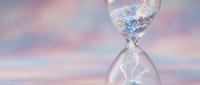 Hourglass with sparkling glitter sand flowing against dreamy pastel sky background symbolizing time passage and magical moments for wellness concepts.
