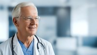 Senior male doctor with stethoscope smiling confidently in modern hospital setting, healthcare professional portrait for medical marketing materials.
