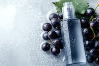 Natural grape extract toner bottle with fresh dark grapes on marble surface. Organic skincare cosmetics with antioxidant properties for anti-aging routine.