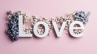 White letters spelling LOVE decorated with delicate blue and white baby's breath flowers on soft pink background, romantic wedding or Valentine's day composition.