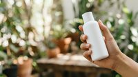 Unbranded white cosmetic bottle held in hand against blurred green foliage background, suitable for skincare, haircare, and beauty product marketing campaigns.