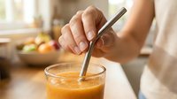 Close-up of hand stirring fresh juice with metal straw in glass, sustainable drinking alternative for beverages and eco-friendly lifestyle.