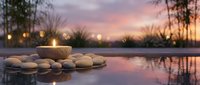 Zen spa stones and candle reflected in calm water at sunset creating peaceful meditation atmosphere for wellness and relaxation retreat.